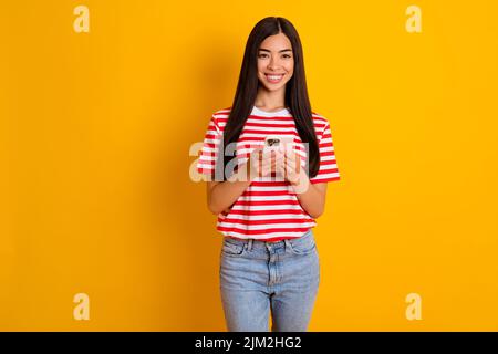 Portrait de jolie fille gaie tenir téléphone sourire torothy porter rouge blanc t-shirt isolé sur fond jaune couleur Banque D'Images