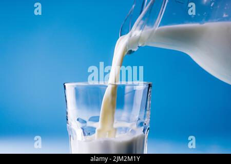 Gros plan du lait versé dans le verre à partir du pot sur fond bleu, espace de copie Banque D'Images