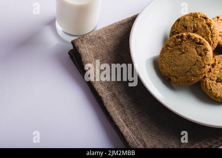 Biscuits dans l'assiette par le verre de lait sur fond blanc, espace de copie Banque D'Images