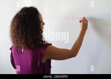 Jeune enseignante caucasienne écrivant la formule sur tableau blanc pendant la classe de mathématiques à l'école Banque D'Images
