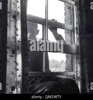 1960s, historique, un homme se penchait hors d'une fenêtre en bois encadrée de guillotine, le nettoyant, Angleterre, Royaume-Uni. Banque D'Images