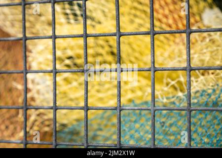 Vue abstraite des filets de pêche colorés à travers la clôture. Mise au point sélective intentionnelle et bokeh d'arrière-plan. Banque D'Images