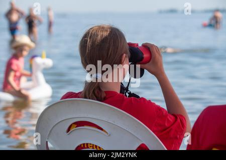 Stralsund, Allemagne. 04th août 2022. Un maître-nageur de la Société allemande de sauvetage (DLRG) est assis sous un parasol sur une chaise dans l'eau de refroidissement lors de cette chaude journée du milieu de l'été au lido, en regardant les baigneurs dans la mer. Credit: Stefan Sauer/dpa/Alay Live News Banque D'Images