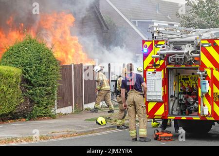 Feu moteur tendre vient d'arriver vue arrière portes ouvertes à la pompe à eau soupapes de commande pompiers travaillant sur maison feu flammes scène de rue Essex Angleterre Royaume-Uni Banque D'Images