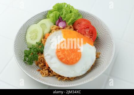 Indomie Goreng ou Mie Goreng, indonésien populaire Instant Noodle. Servi avec un œuf de poule, de la tomate et du concombre. Sur la table blanche Banque D'Images