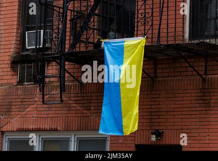 Un drapeau ukrainien suspendu d'une fuite au feu sur le côté d'un bâtiment en briques rouges dans la ville de New york, montrant la solidarité avec l'Ukraine Banque D'Images