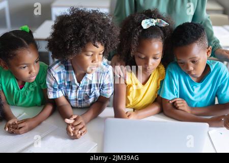 Étudiants afro-américains du primaire regardant dans un ordinateur portable tout en étant assis à un bureau pendant un cours d'informatique Banque D'Images