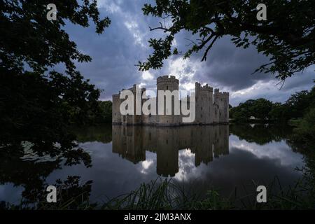 Château de Bodiam dans l'est du Sussex au coucher du soleil avec le château reflété dans les douves environnantes et encadré par des arbres Banque D'Images