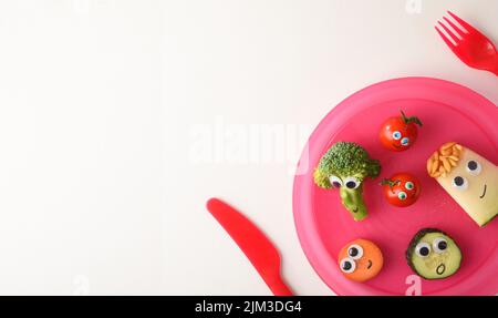 Filet de sécurité avec une jolie assiette de fruits et légumes amusants servis pour les enfants avec des couverts rouges pour les enfants sur une table blanche. Vue de dessus. Banque D'Images