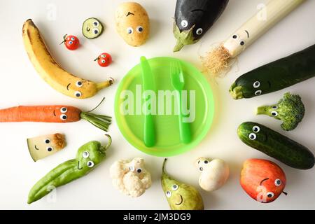 Filet de sécurité avec une jolie assiette de fruits et légumes amusants servis pour les enfants avec des couverts rouges pour les enfants sur une table blanche. Vue de dessus. Banque D'Images