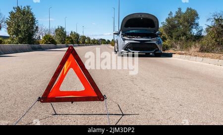 Voiture avec des problèmes et un triangle rouge pour avertir les autres usagers de la route. Une voiture brisée avec capot ouvert. Concept d'accident sur la rue. Banque D'Images