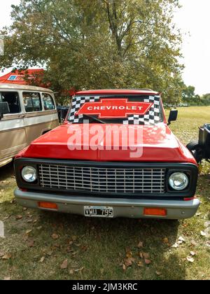 Chevrolet badge logo on windscreen of an old red pickup truck circa 1960. Green grass nature. Front view. Grill. Classic car show. Copyspace Stock Photo