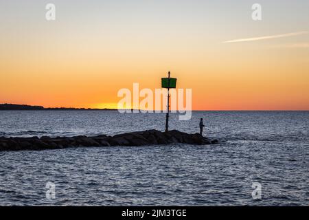Une belle photo d'un homme debout sur le bord d'une jetée de roche contre le ciel de crépuscule au coucher du soleil à Martha's Vineyard Island, Massachusetts, États-Unis Banque D'Images