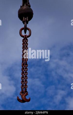 Les chaînes avec des crochets accrochés à la grue contre un ciel nuageux Banque D'Images
