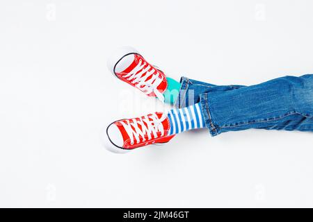Enfant portant différentes paires de chaussettes. Pieds d'enfant dans des chaussettes et des baskets rouges mal assorties sur fond blanc. Journée des chaussettes impaires, semaine anti-intimidation Banque D'Images