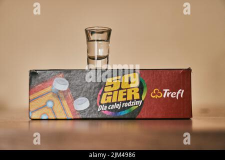 Un verre de vodka sur une boîte de marque Trefl avec cinquante jeux sur une table brillante Banque D'Images