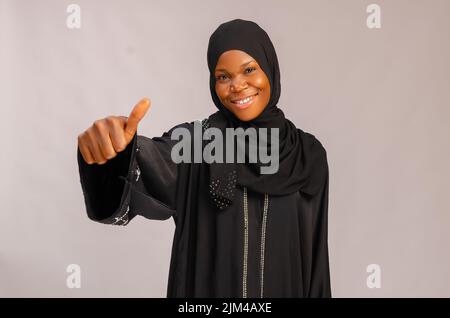 Une femme musulmane africaine souriante souriant souriant alors qu'elle se levant le pouce isolée sur fond gris Banque D'Images