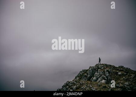 La personne debout sur le sommet de la montagne contre le ciel gris nuageux. Randonnée, Monténégro. Banque D'Images