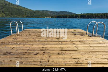 Jetée en bois avec échelle en métal dans la mer, le lac, l'eau. Quai de baignade avec échelle en métal sur le lac bleu calme à la journée ensoleillée sur la station idyllique au culte Banque D'Images