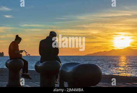 Vue de la silhouette d'une personne à l'aide d'un smartphone au coucher du soleil. Femme et homme utilisant des téléphones intelligents assis sur la plage à Sunset-24 juillet,2022-Vancouver C.-B. C Banque D'Images