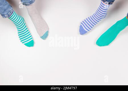 Enfant portant différentes paires de chaussettes. Pieds d'enfant dans des chaussettes mal assorties assis sur fond blanc. Journée des chaussettes impaires, semaine anti-intimidation, syndrome de Down Banque D'Images