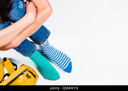 Enfant portant différentes paires de chaussettes. Pieds d'enfant dans des chaussettes mal assorties assis sur fond blanc. Journée des chaussettes impaires, semaine anti-intimidation, syndrome de Down Banque D'Images