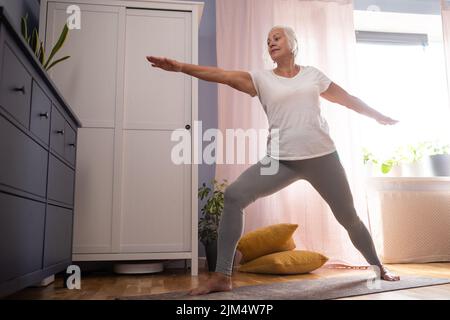 femme senior faisant du yoga asana dans le salon. Banque D'Images