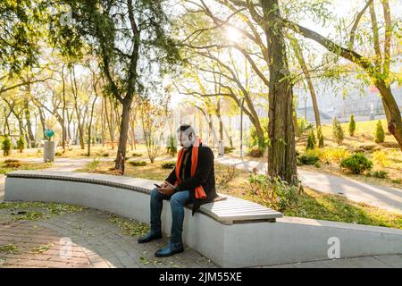 Homme à barbe noire utilisant un téléphone portable assis sur un banc au parc Banque D'Images
