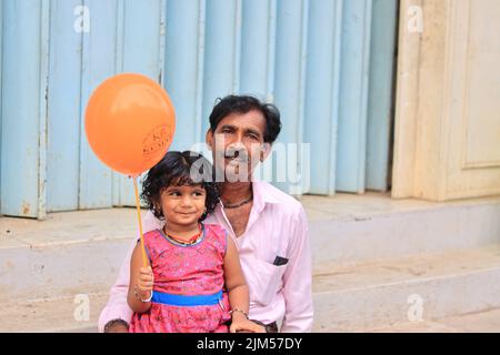 Un grand-père portant sa petite-fille tenant un ballon dans ses bras dans une foire d'amusement de village. Banque D'Images