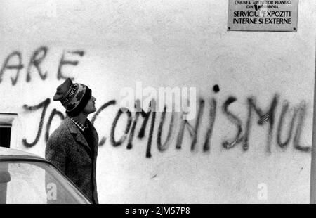 Bucarest, Roumanie, janvier 1990. Quelques jours après la Révolution anticommuniste roumaine de 1989, un homme passe devant un bâtiment où quelqu'un peint « le bas avec le communisme », un acte impensable un mois auparavant. Banque D'Images