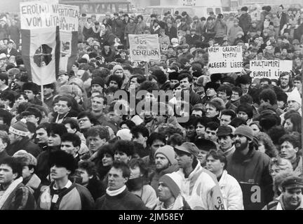 Bucarest, Roumanie, janvier 1990. Rassemblement sur la place de l'Université après la révolution roumaine de 1989. Les gens se rassembleraient tous les jours pour protester contre les anciens dirigeants communistes qui ont pris le pouvoir après la Révolution. Le drapeau roumain avec l'emblème socialiste coupé était un symbole anticommuniste pendant la révolution. Bannières disant « nos héros, nous ne vous oublierons jamais », « la liberté triomphera », « la nouvelle censure sera la nôtre », « nous voulons des garanties pour des élections libres », « Merci, radio Free Europe ». Banque D'Images