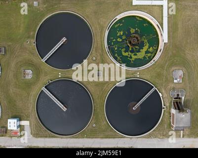 Vue aérienne directe au-dessus d'une station de traitement des eaux usées, centrée au-dessus de quatre réservoirs de sédimentation ronds. Banque D'Images