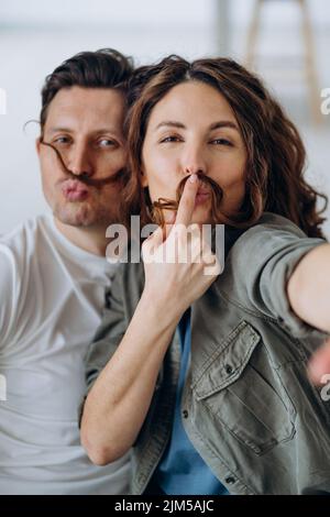 Les jeunes mariés jouent et posent pour faire des moustaches avec des cheveux bruns et des baiser en souriant pour les selfies via un smartphone Banque D'Images