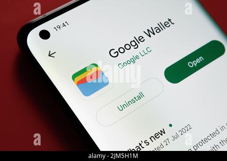 L'application Google Wallet apparaît dans Google Play Store sur l'écran du smartphone, sur fond rouge. Gros plan avec mise au point sélective. Stafford, Royaume-Uni Banque D'Images