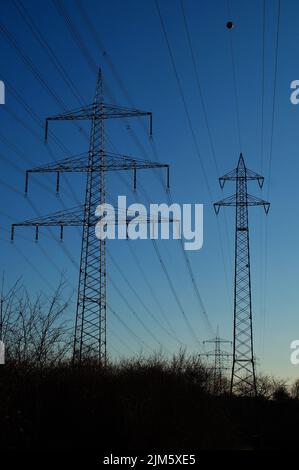 Silhouettes de pylônes haute tension à côté de l'autoroute A5 à Francfort-Riedberg, en Allemagne, contre le ciel bleu du soir. Banque D'Images