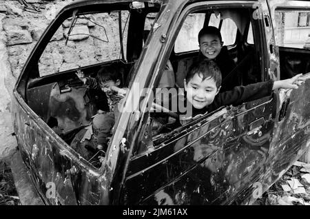 Photo en niveaux de gris d'un groupe d'enfants jouant à l'intérieur d'une vieille voiture brûlée à Istanbul, Turquie Banque D'Images