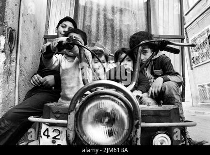 Photo en niveaux de gris d'un groupe d'enfants assis et jouant sur une vieille automobile à Istanbul, Turquie Banque D'Images