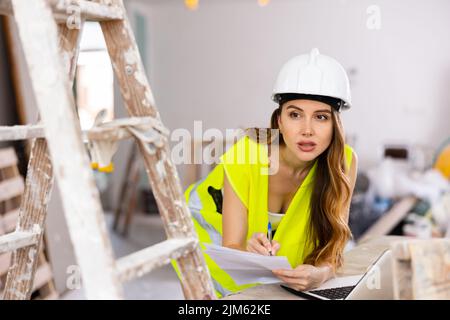 Femme architecte travaillant avec un ordinateur portable et des papiers dans la maison en cours de reconstruction Banque D'Images