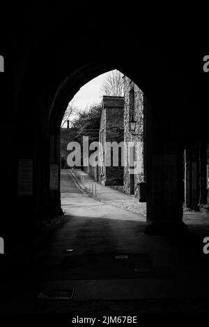 Une photo verticale en niveaux de gris d'une allée avec une arche menant à une rue avec de vieux bâtiments en pierre à Durham Banque D'Images