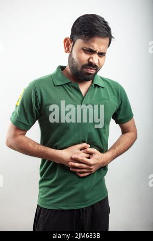 Jeune homme beau sur fond blanc qui embrase sa blessure au coude dans la douleur avec l'expression criante. Banque D'Images