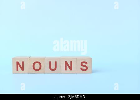 Concept de nom ou de nom dans l'enseignement de la grammaire anglaise. Jeu de mots croisés en bois posé sur fond bleu. Banque D'Images