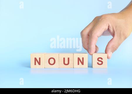 Concept de nom ou de nom dans l'enseignement de la grammaire anglaise. Jeu de mots croisés en bois posé sur fond bleu. Banque D'Images