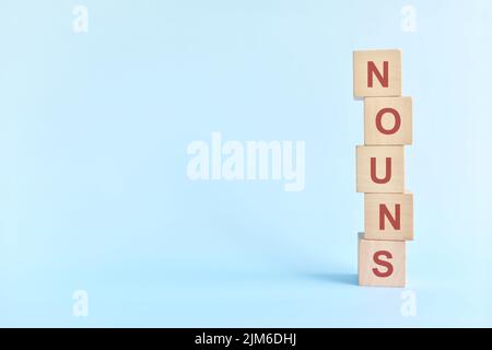 Concept de nom ou de nom dans l'enseignement de la grammaire anglaise. Jeu de mots croisés en bois posé sur fond bleu. Banque D'Images