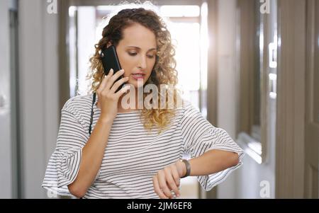 N'attendez pas plus de temps, le temps ne vous attend pas. Une jeune femme d'affaires utilisant un smartphone et vérifiant l'heure tout en marchant dans un moderne Banque D'Images