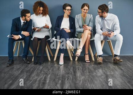 Groupe de gens d'affaires en réseau sur des téléphones, des tablettes numériques et des médias sociaux, en attente dans la file d'attente. Équipe diversifiée de collègues en file d'attente, parlant Banque D'Images