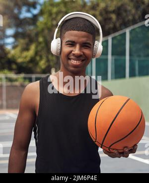 Jouez avec tout votre cœur. Portrait d'un jeune sportif qui écoute de la musique tout en jouant au basket-ball sur un terrain de sport. Banque D'Images