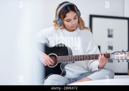 Laissez votre passion devenir votre but. Une jeune femme portant des écouteurs tout en jouant de la guitare à la maison. Banque D'Images