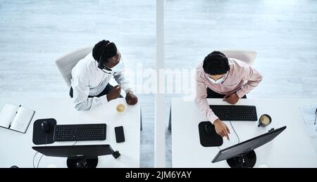 S'aider mutuellement à distance de sécurité. Prise de vue en grand angle de deux agents de centre d'appels travaillant ensemble dans un bureau. Banque D'Images