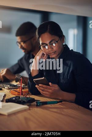 Votre produit sera prêt à être pris en charge demain matin. Un jeune technicien utilisant un smartphone tout en réparant du matériel informatique. Banque D'Images