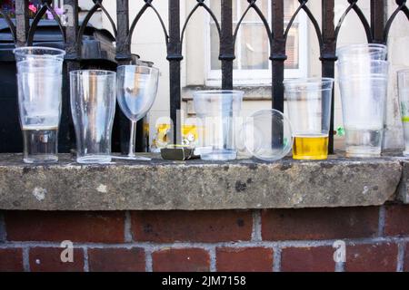 Un gros plan de gobelets en plastique et en verre sur la surface du mur de briques contre les rails métalliques. Banque D'Images